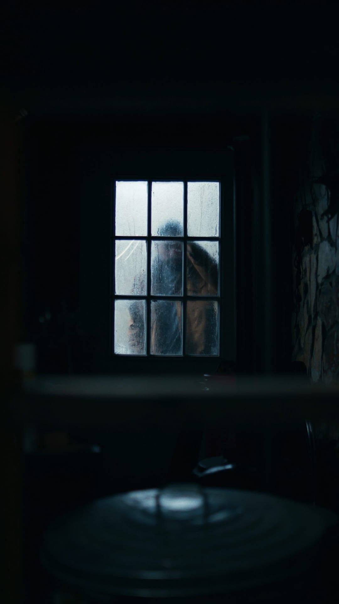 figure behind a fogged window in a dark blue room
