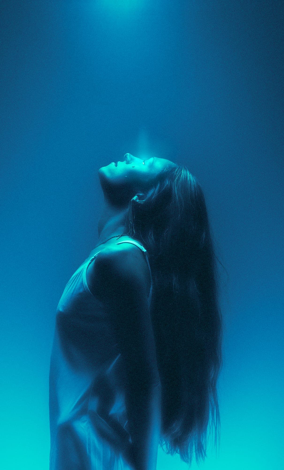 figure tilting her head back into a beam of blue light